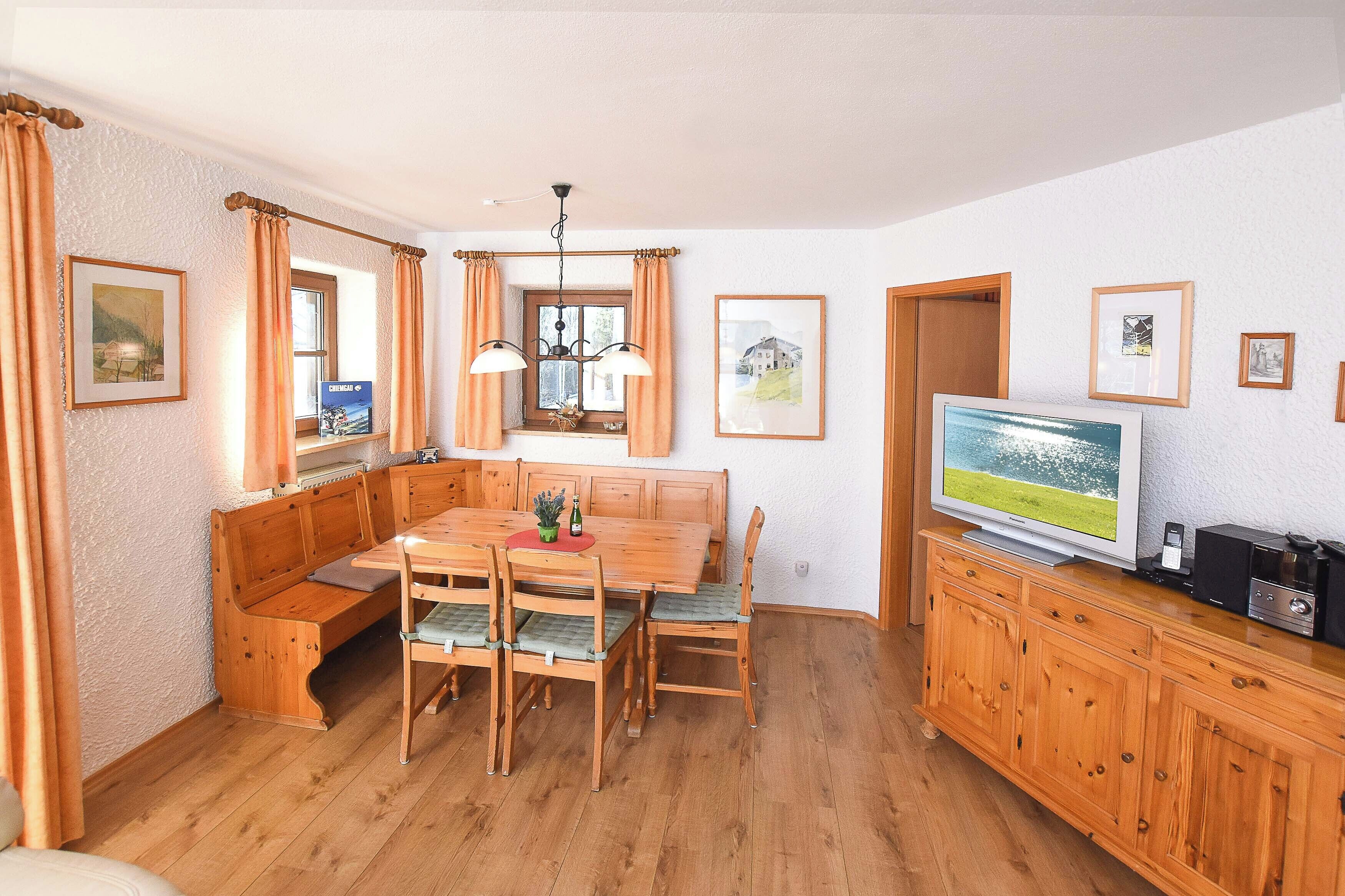 A dining area with a wooden table, chairs, a bench, and a television on a wooden cabinet.