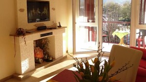 A living room with a fireplace, a television, and a balcony with a table and chairs. - Exclusive vacation apartment with mountain view, 50sqm, 1 bedroom, winter garden (Bad Reichenhall)