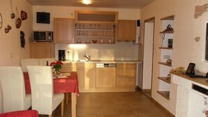 A compact kitchen with wooden cabinets, a microwave, and a dining area with a red tablecloth. - Exclusive vacation apartment with mountain view, 50sqm, 1 bedroom, winter garden (Bad Reichenhall)