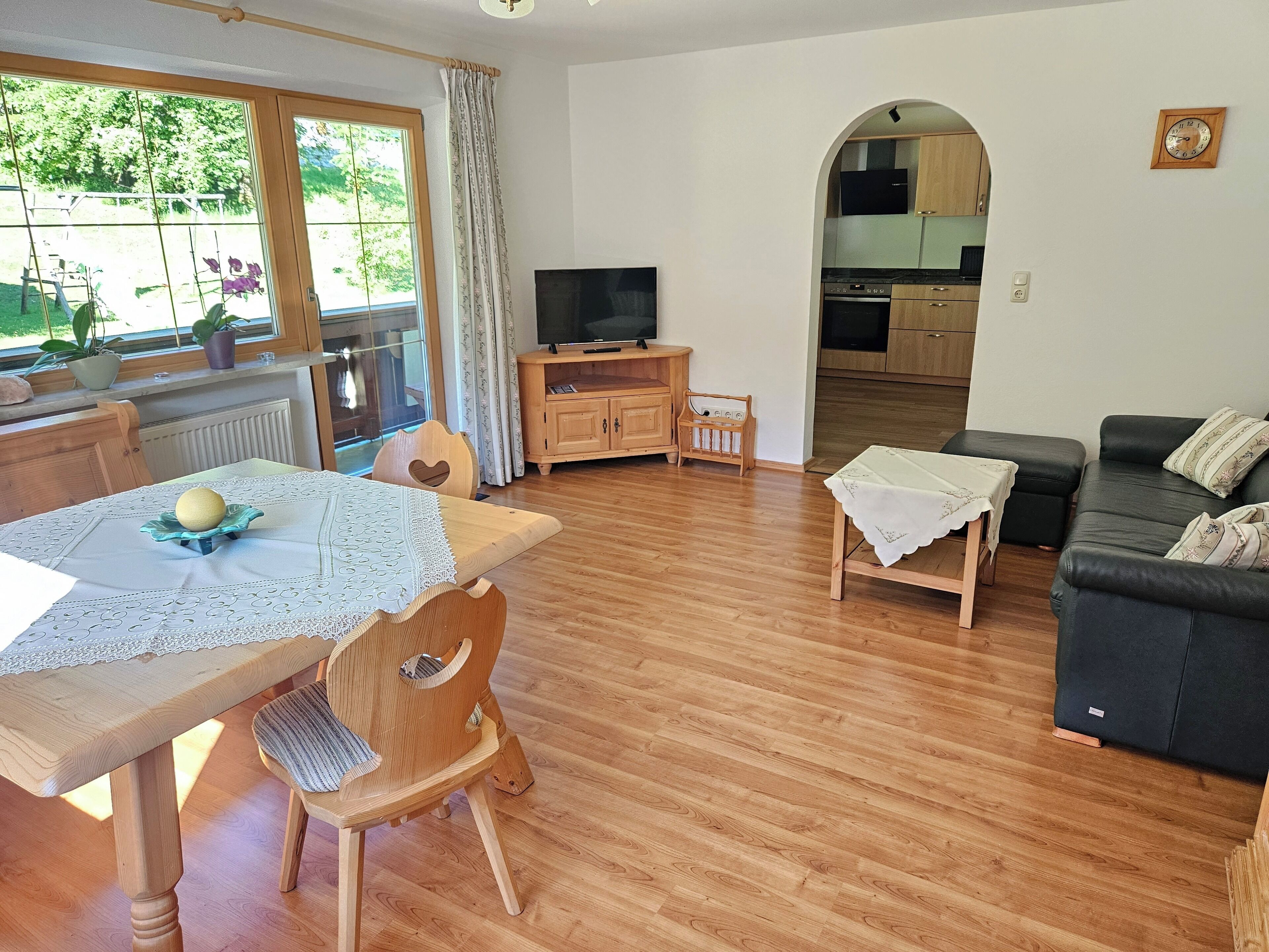 Un salón acogedor con una mesa de comedor de madera, un sofá de cuero negro y un televisor.