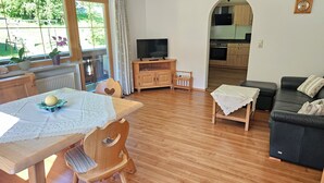 Uma sala de estar acolhedora com uma mesa de jantar de madeira, um sofá de couro preto e uma televisão.
