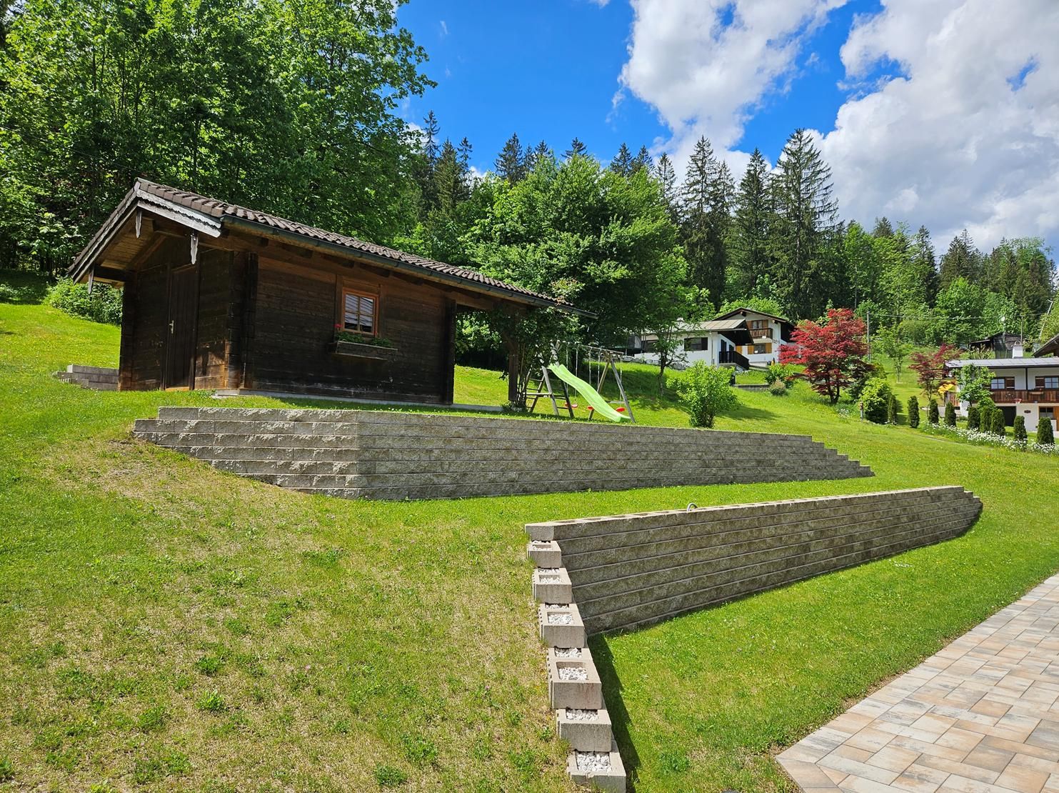 A wooden cabin with a stone staircase leading up to it, surrounded by lush greenery and trees.