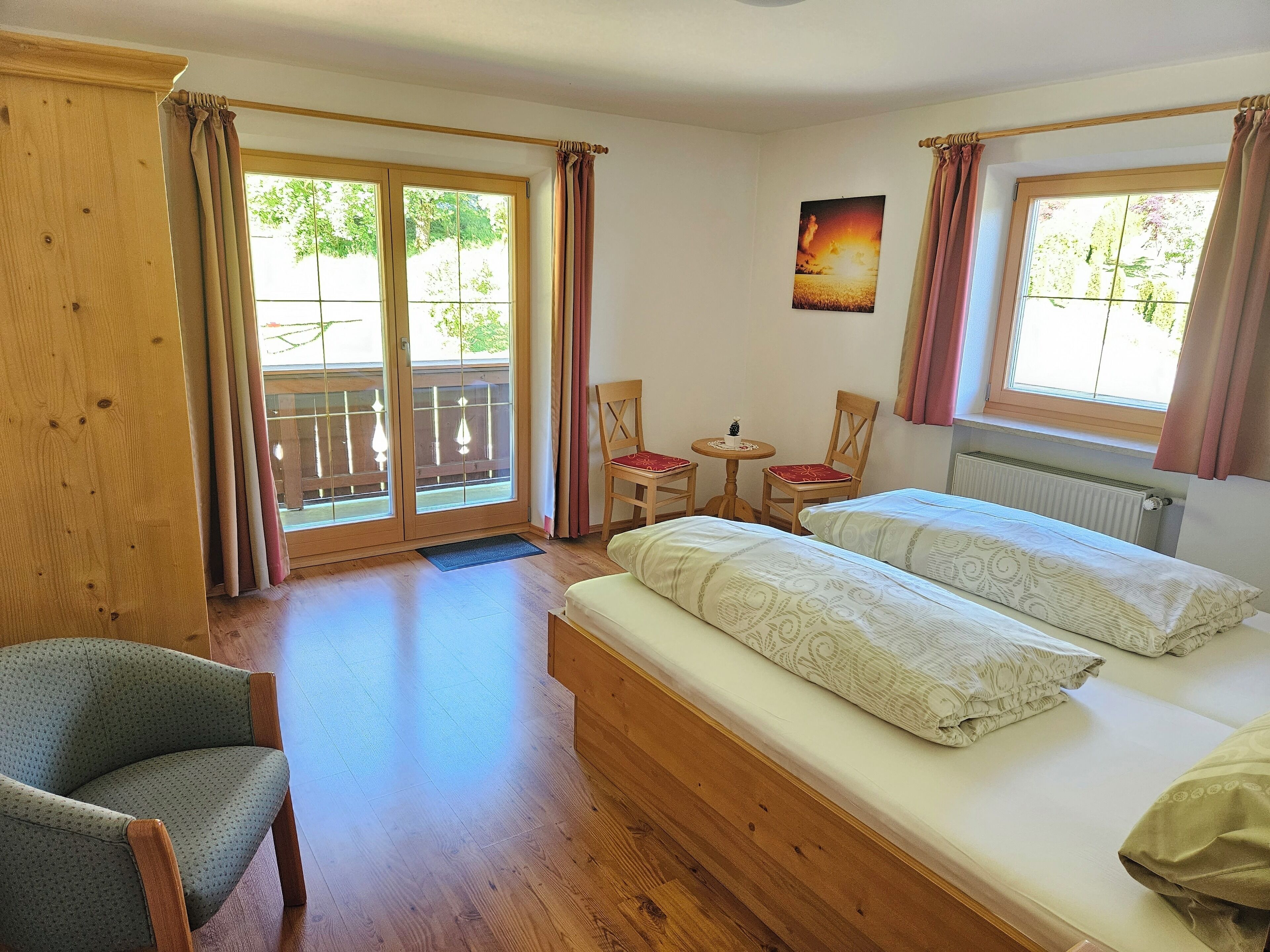 Ein Zimmer mit einem Bett, einem Sessel, einem kleinen Tisch und einem Fenster mit Vorhängen.