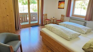 Quarto com cama, uma cadeira, uma mesa pequena e janela com cortinas.