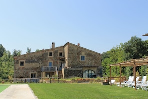 Un bâtiment rustique en pierre, doté d’un balcon, d’un chemin pavé et d’un espace extérieur aménagé pour s’asseoir.