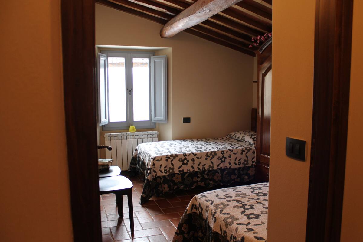 Un dormitorio con dos camas, una ventana, un radiador y una pequeña mesa.
