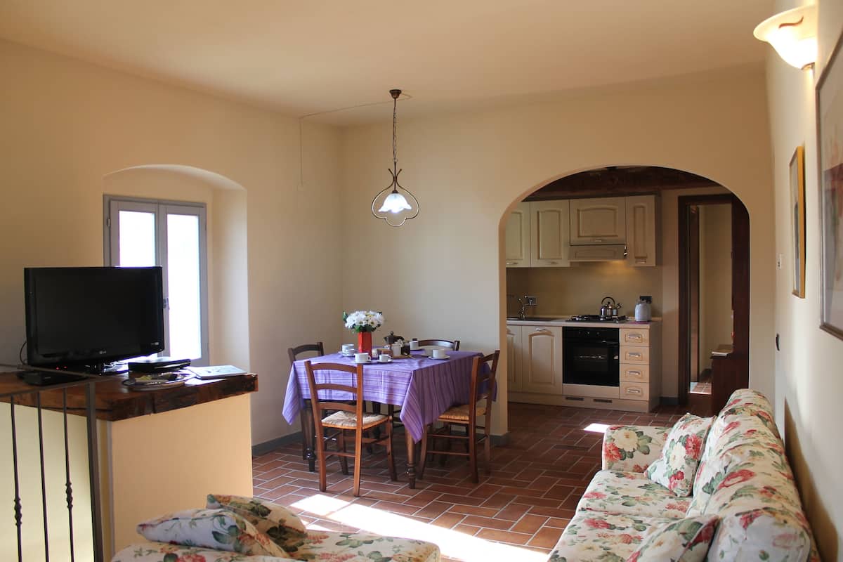 Un comedor con una mesa dispuesta para cuatro personas, un televisor sobre un mueble bajo y un sofá al frente.