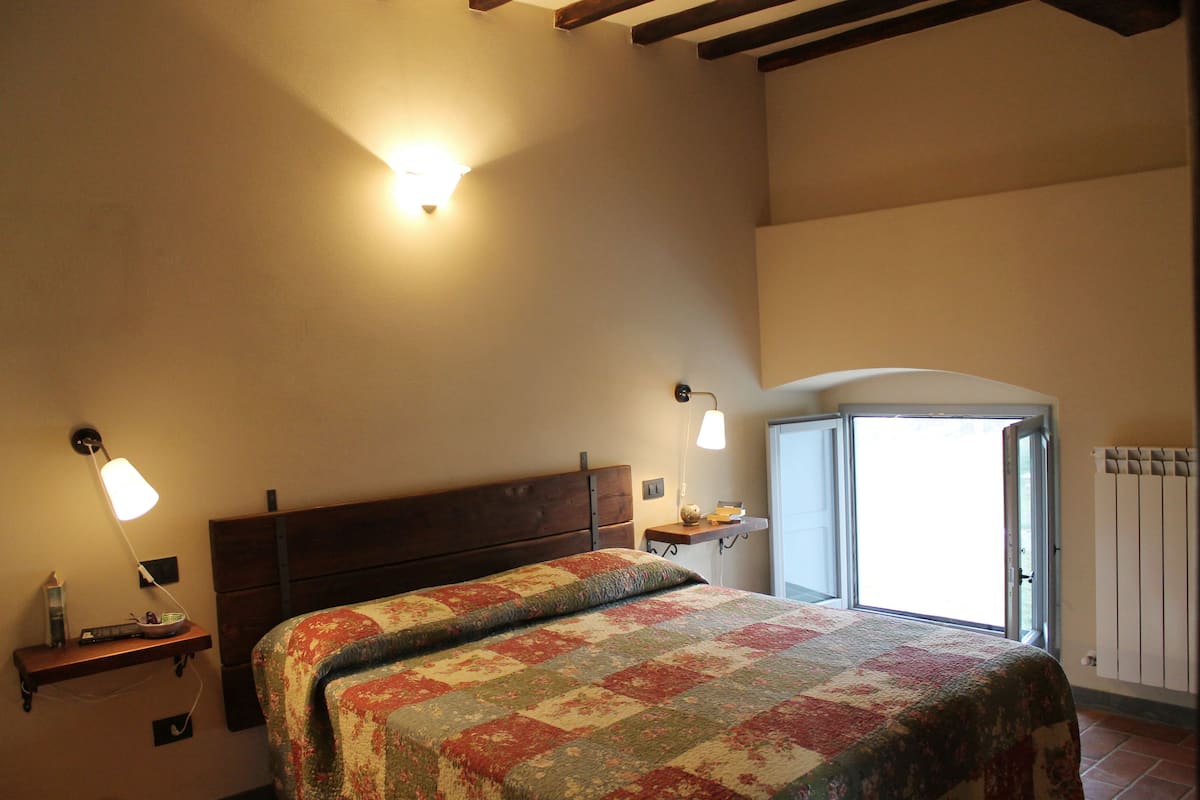 Un dormitorio con cama, lámparas de noche, mesita de noche, ventana y radiador.