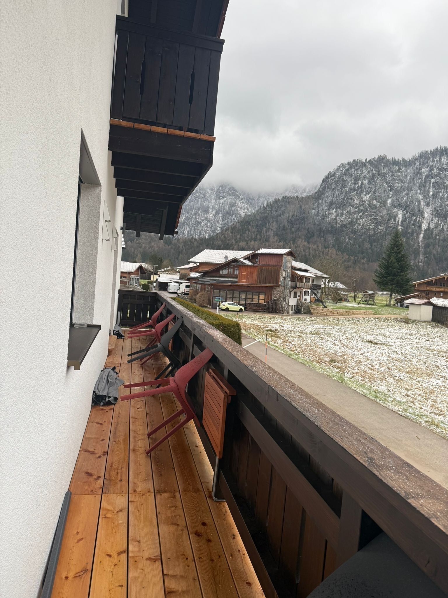 A wooden deck with a view of snow-covered mountains and a village.