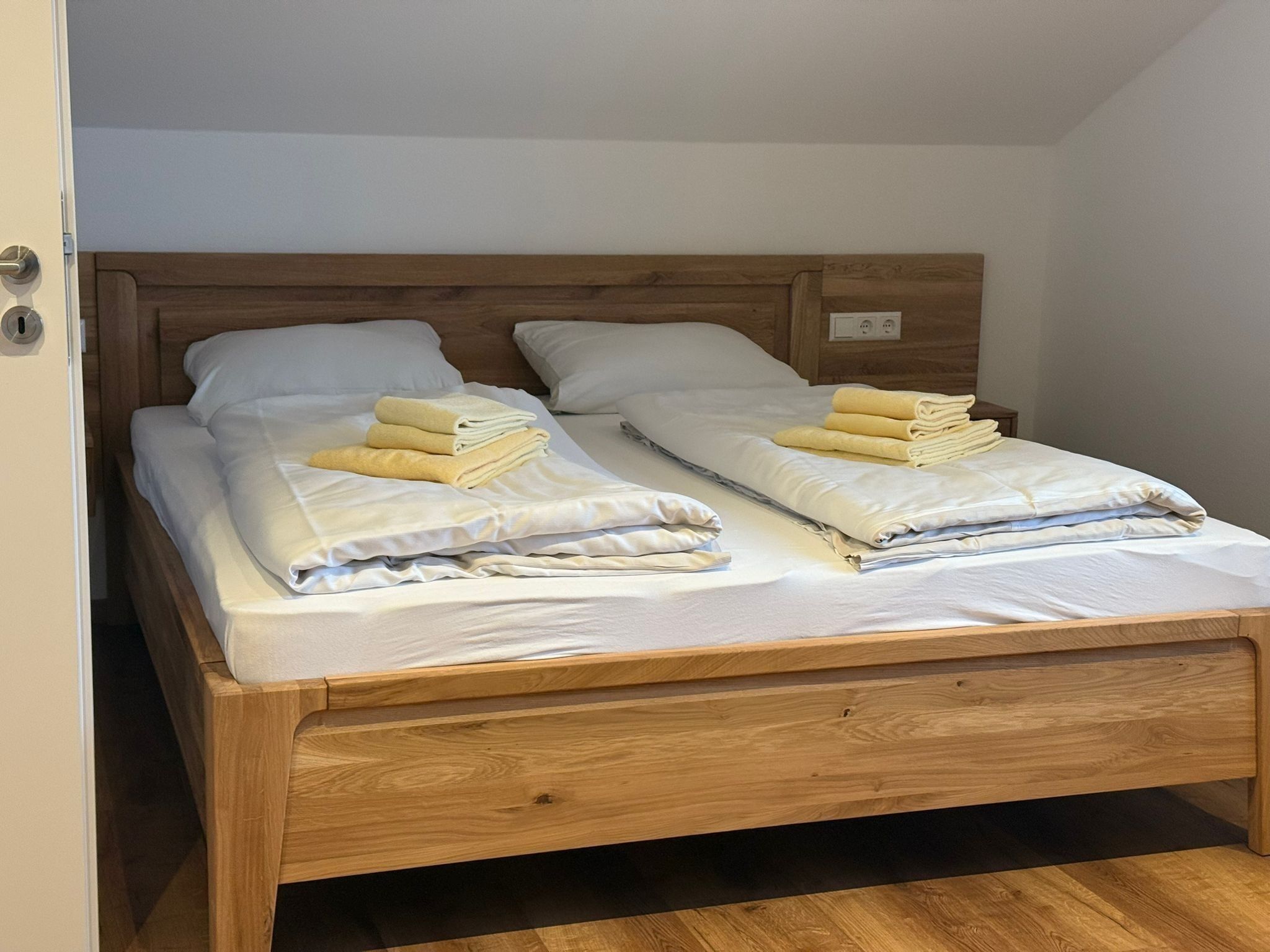 A double bed with wooden headboard and footboard, white linens, and neatly folded towels.
