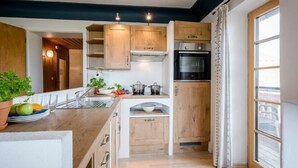 A modern kitchen with wooden cabinets, a built-in oven, and a window with curtains. - Vacation apartment Hartsee 52sqm, 2 bedrooms, fireplace, balcony (Eggstätt)