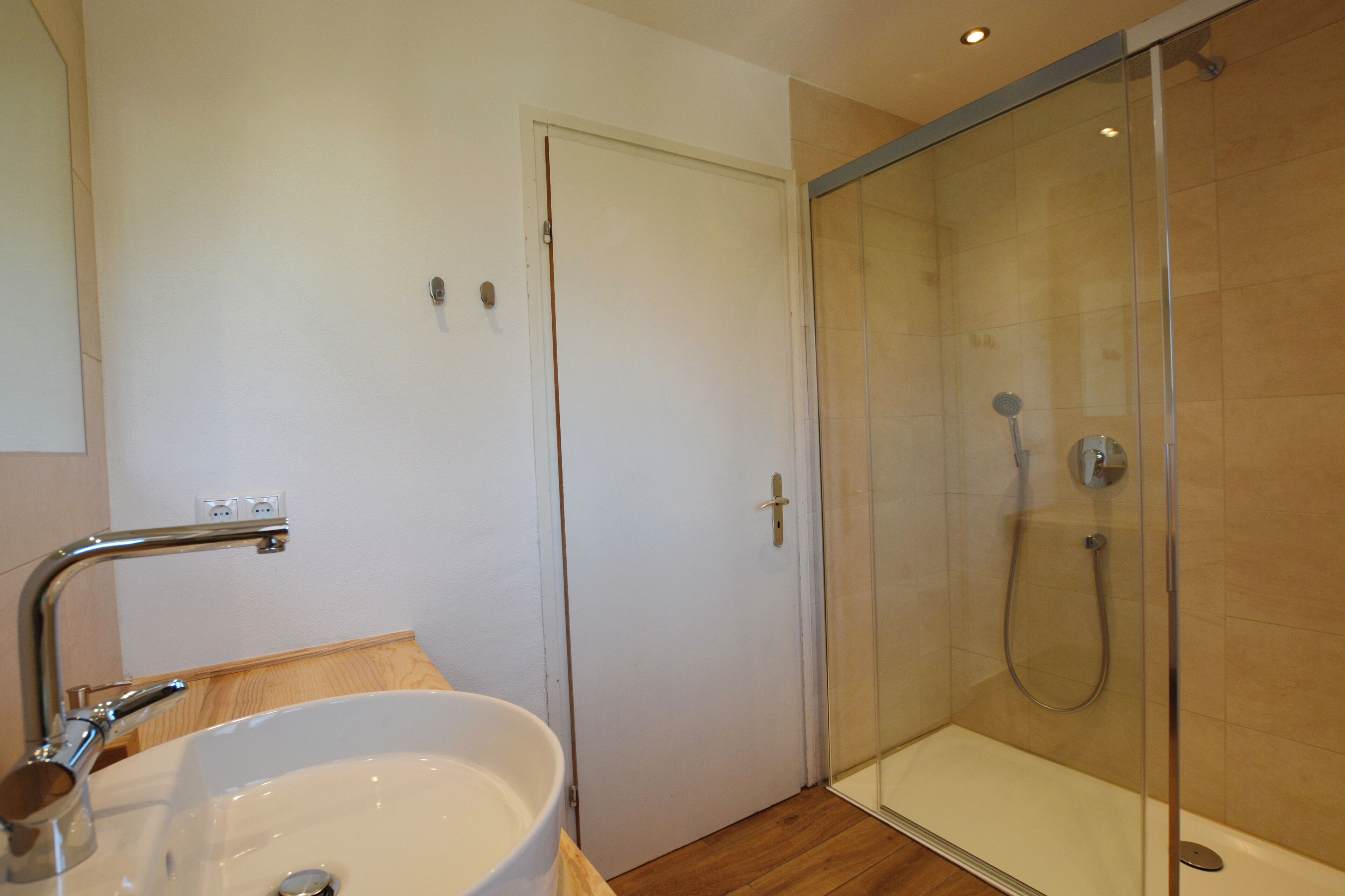 A bathroom with a white sink, a glass shower enclosure, and a wooden floor.