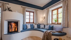 A cozy living room with a built-in fireplace, a curved seating area with cushions, and two windows with curtains. - Vacation apartment Hartsee 52sqm, 2 bedrooms, fireplace, balcony (Eggstätt)