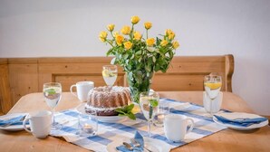 A dining table set with a bundt cake, a vase of yellow flowers, and several glasses of water and white tea. - Vacation apartment Hartsee 52sqm, 2 bedrooms, fireplace, balcony (Eggstätt)