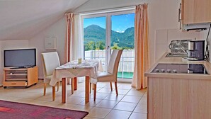 Una habitación con televisor, una mesa de comedor, sillas, una zona de cocina y un balcón con vista a la montaña.