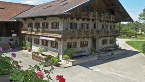 A traditional chalet with a sloped roof, multiple balconies with flower boxes, and a stone facade. - Ferienwohnung Bauernhaus Hochgernblick (Grassau)