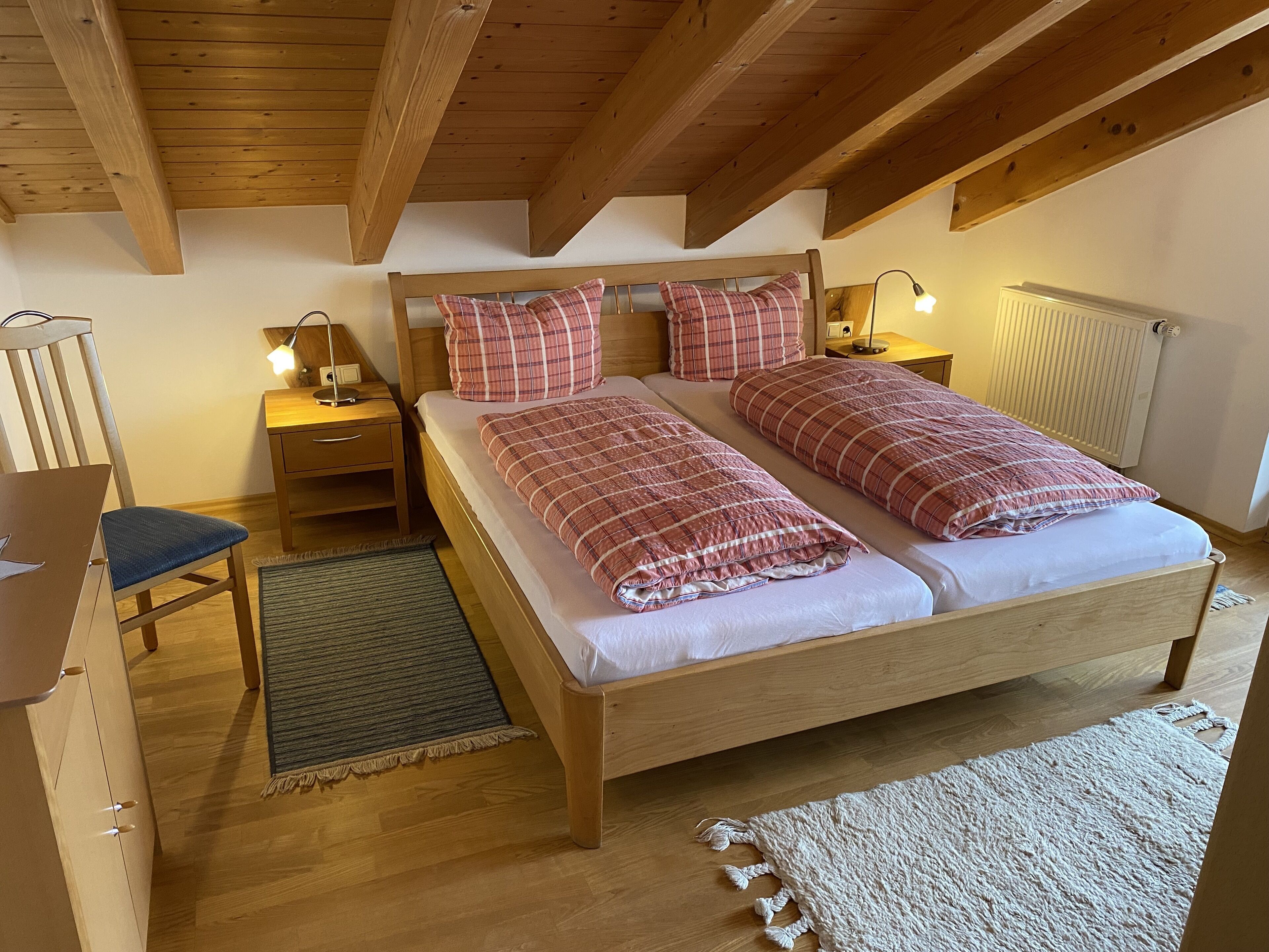 Un dormitorio con estructura de madera, una cama doble, dos mesitas de noche con lámparas, una silla y un escritorio.