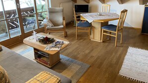 Een gezellige kamer met een houten plafond, een eettafel met stoelen, een bank en een raam met uitzicht op een terras.