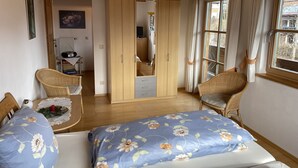 Een slaapkamer met een bed, twee rieten stoelen, een kledingkast en een raam met gordijnen.