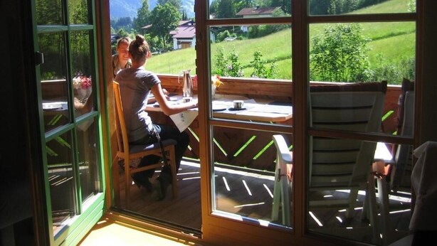 Een kamer met een grote glazen deur die uitkomt op een buitengebied met uitzicht op een groen landschap en bergen.