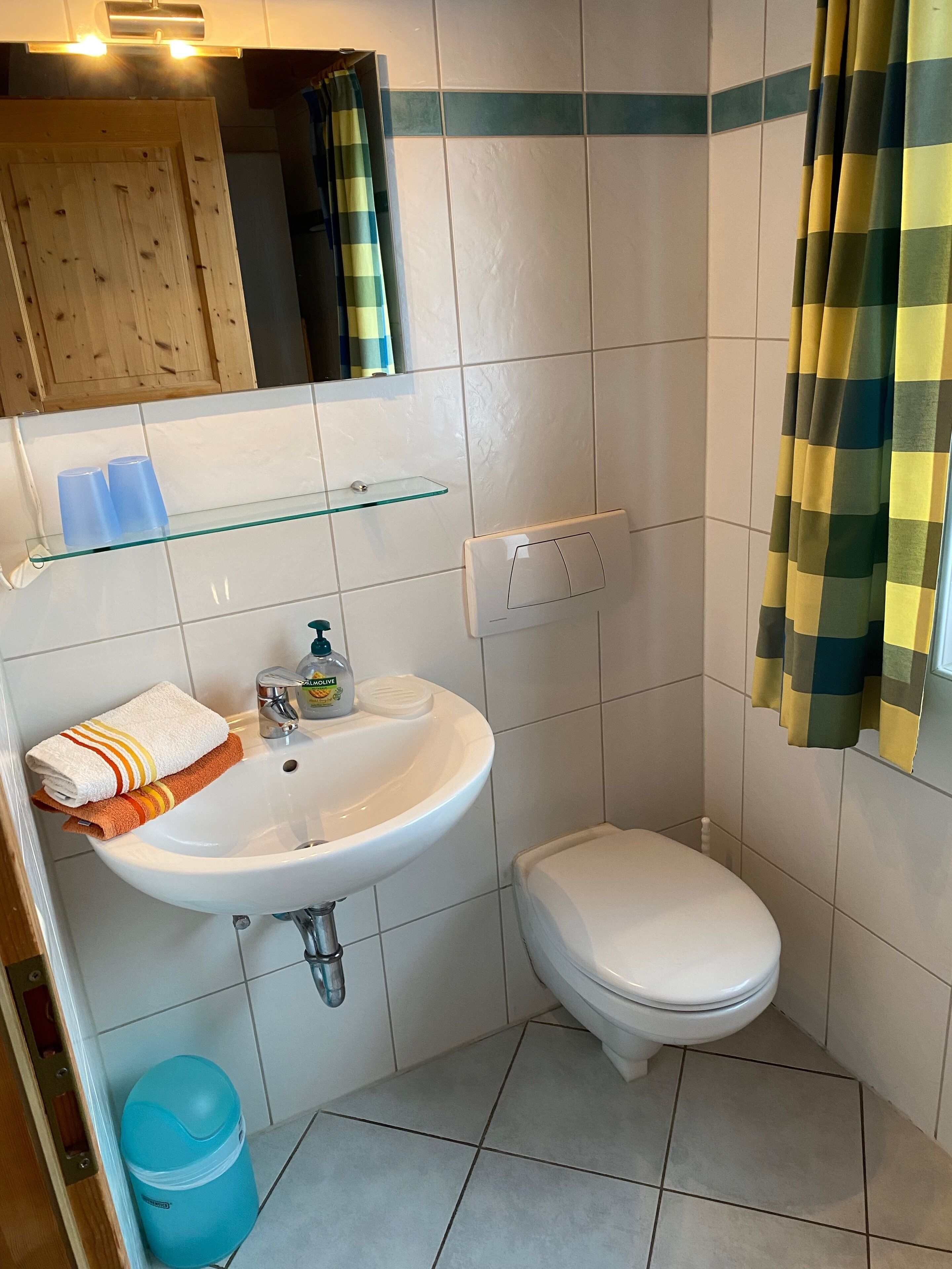 Un baño pequeño con un lavabo blanco, un inodoro y un estante de vidrio sobre el lavabo.