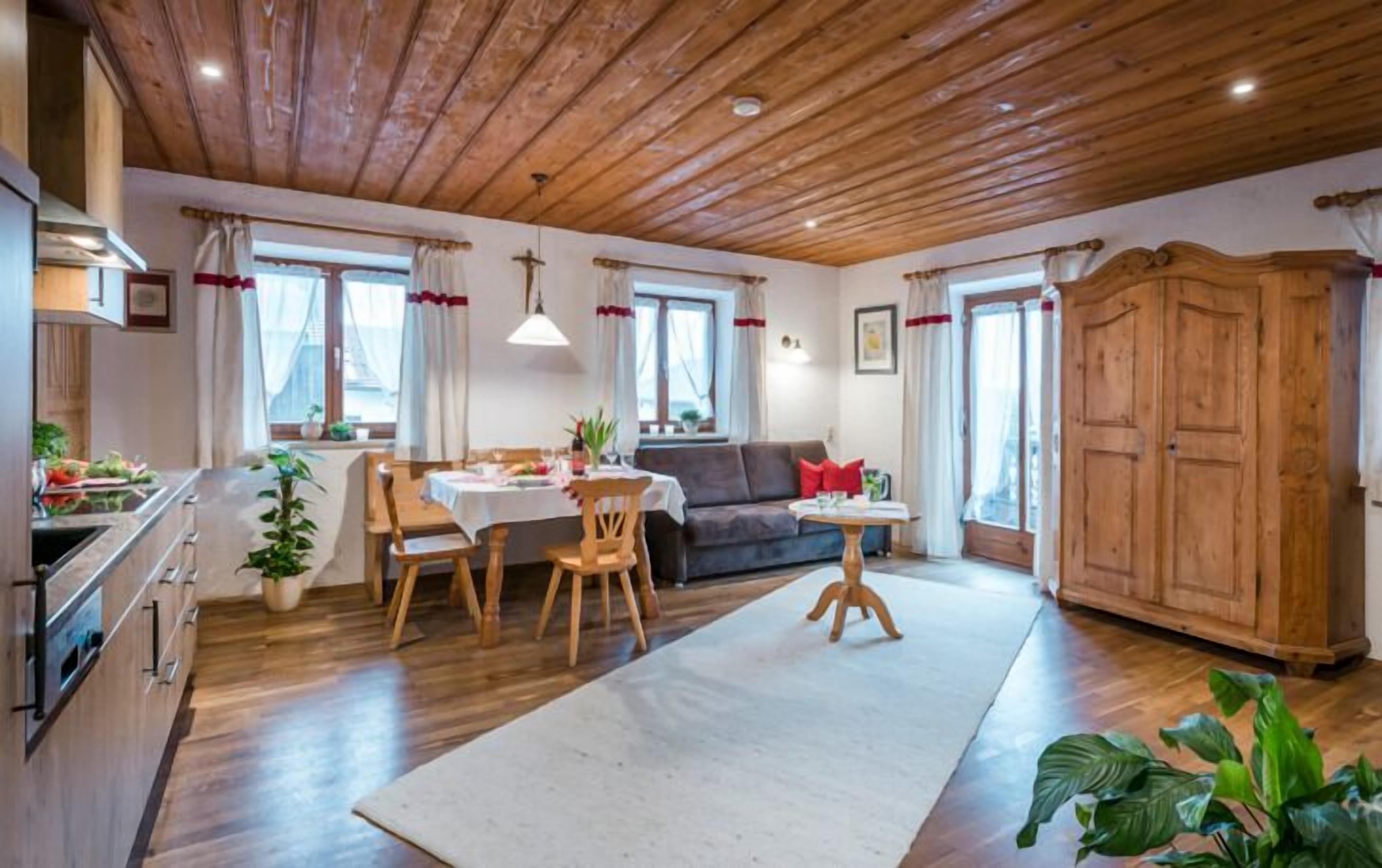 A cozy living room with a dining area, wooden ceiling, and a large wooden wardrobe.