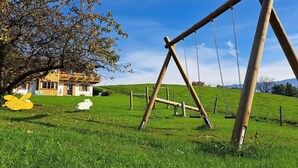 Um balanço de madeira num campo gramado, com uma casa ao fundo.