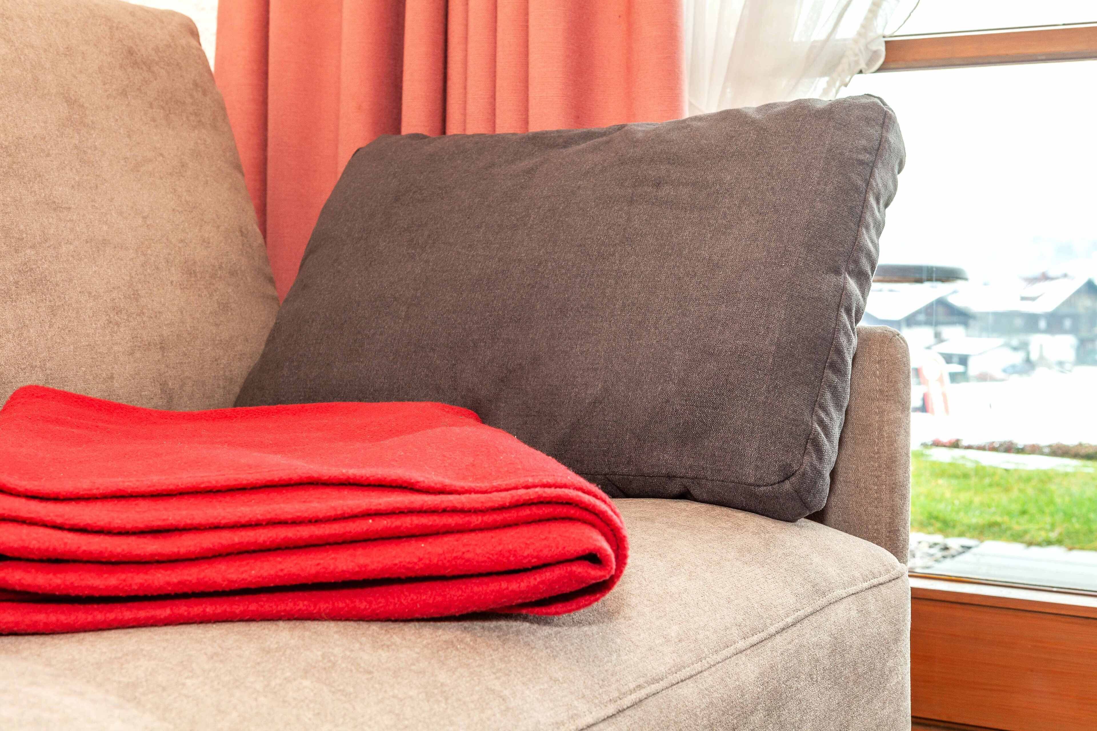 Un canapé beige avec un coussin gris foncé et une couverture rouge.