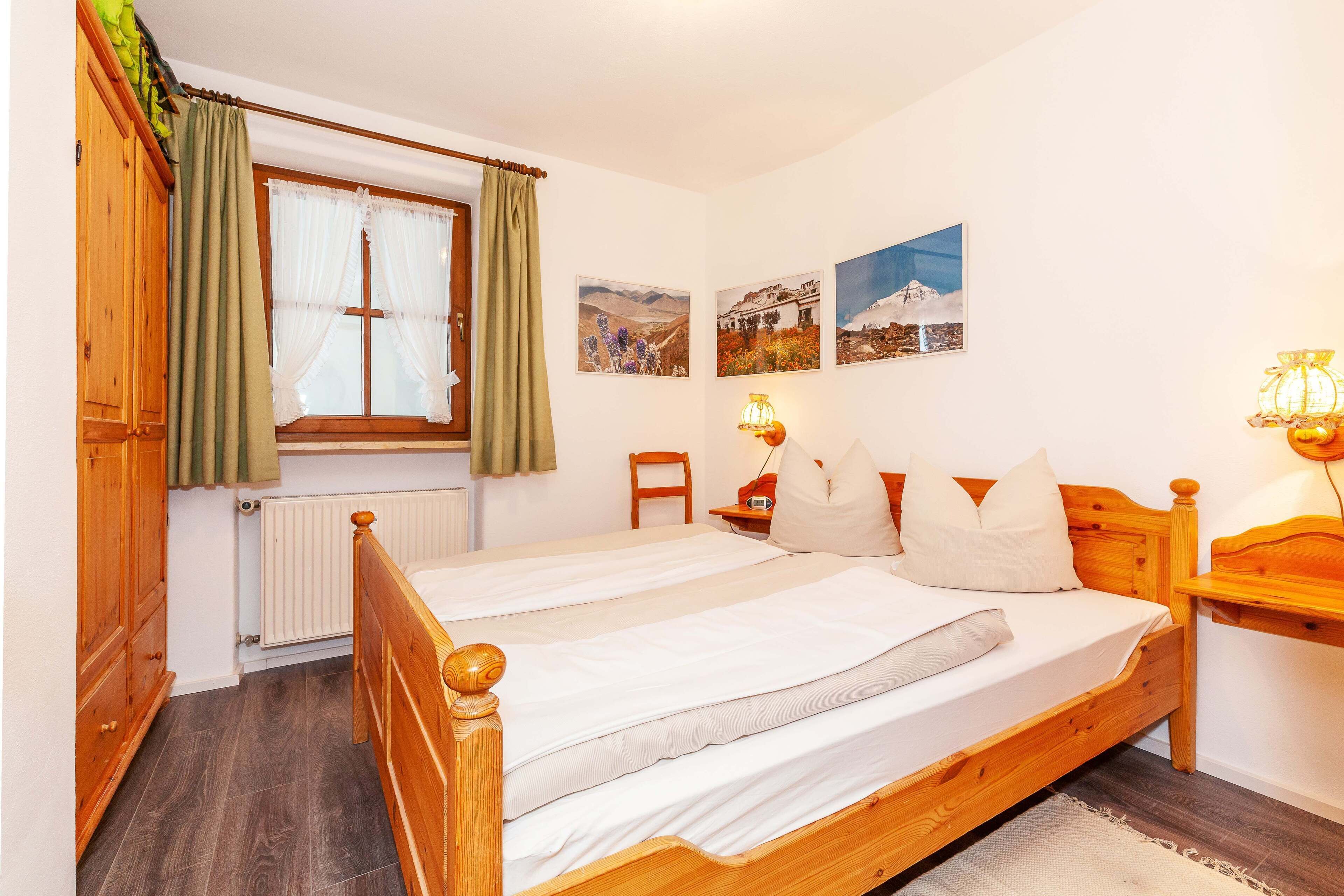 A bedroom with a wooden bed, a radiator, a window with curtains, a chair, and wall-mounted lamps.