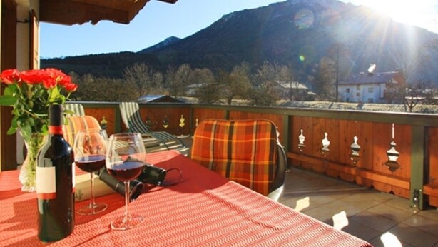 Una mesa con una botella de vino y copas, una silla a cuadros y vistas de una montaña.