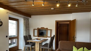 Una sala de estar acogedora con techo de madera, una mesa de comedor con sillas, un sofá marrón con cojines verdes y una ventana con cortinas.