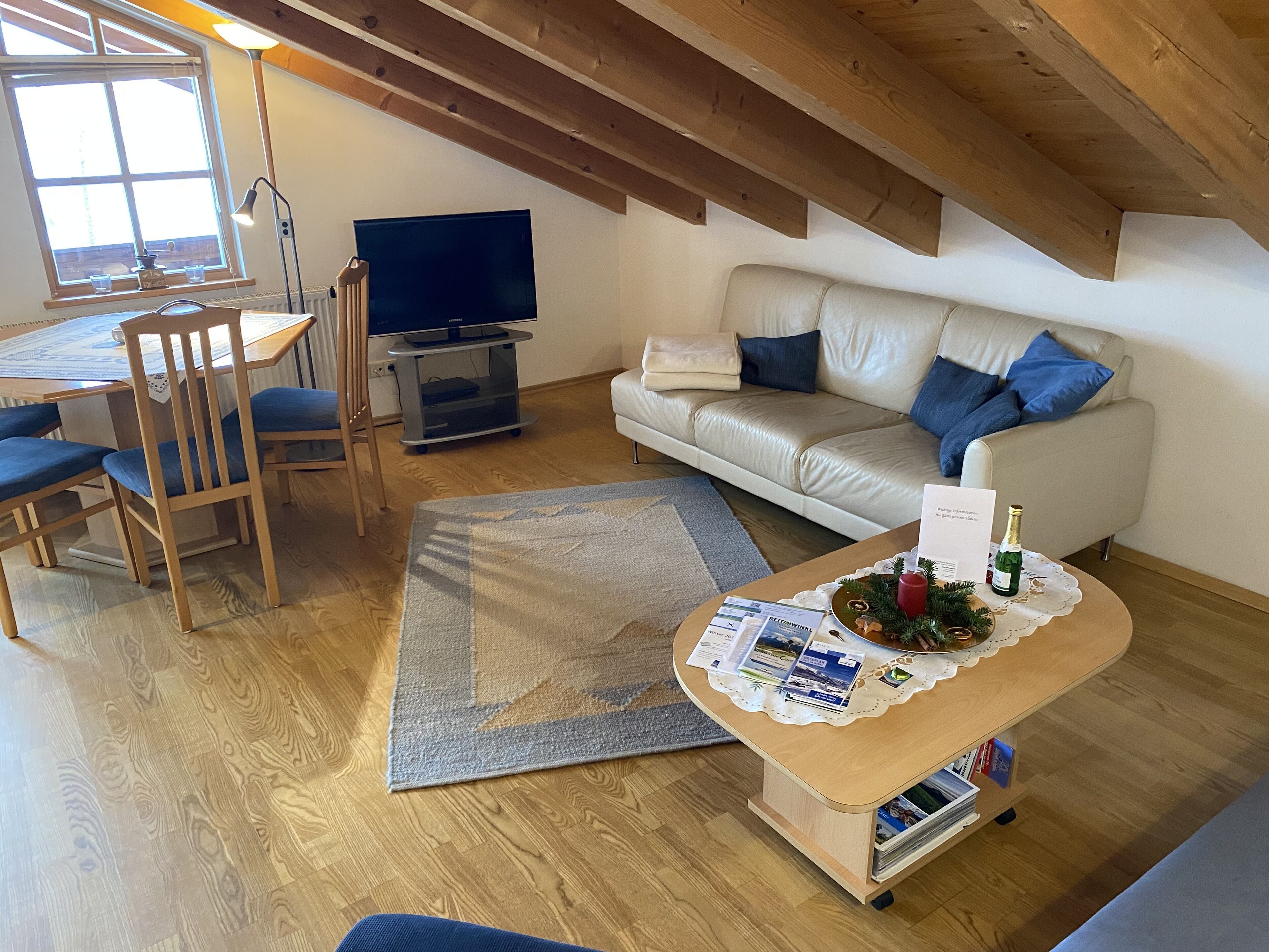 Uma sala de estar acolhedora com teto de madeira, um sofá, uma mesa de centro com revistas, uma TV e uma área de jantar com cadeiras e uma mesa.
