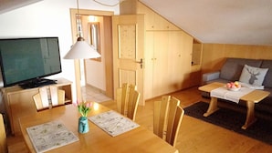 A cozy room with a wooden dining table, chairs, a television, a lamp, and a sofa with a cushion. - Vacation apartment Gipfelruhe (Reit im Winkl)
