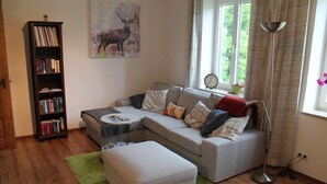 En stue med en grå sofa, en matchende skammel, en bogreol og et billede af et rådyr på væggen.