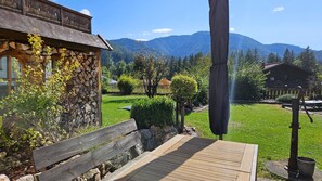 A wooden deck with a bench, a stone wall with stacked wood, and a view of a mountain range. - Komfortable Ferienwohnung, 85 qm, 2 sep. Schlafzimmer und Küche (Reit im Winkl)