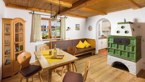A cozy room with wooden furniture, a green and white fireplace, and a dining area with a yellow tablecloth. - Ferienhaus für 2-4 Personen (Berchtesgaden)