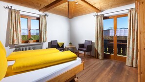 A bedroom with a wooden bed, two chairs, a small table, and a view through a window. - Ferienhaus für 2-4 Personen (Berchtesgaden)