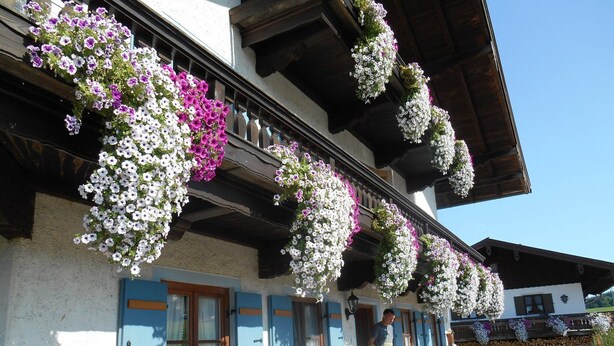 A traditional chalet with flower baskets hanging from the balcony, outdoor seating, and a stone patio. - No. 2 Holiday apartment Hörndlwand 70sqm, balcony, 2 bedrooms, 1 bed-sitting room (Ruhpolding)