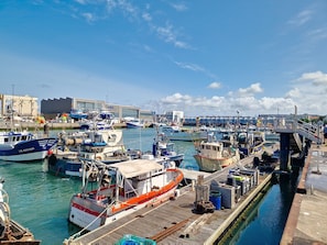 Uma marina com vários barcos atracados, um píer de madeira e um edifício com sinalização ao fundo.