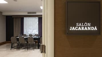 A conference room with a table and chairs, a sign reading "SALÓN JACARANDA," and a window with curtains.