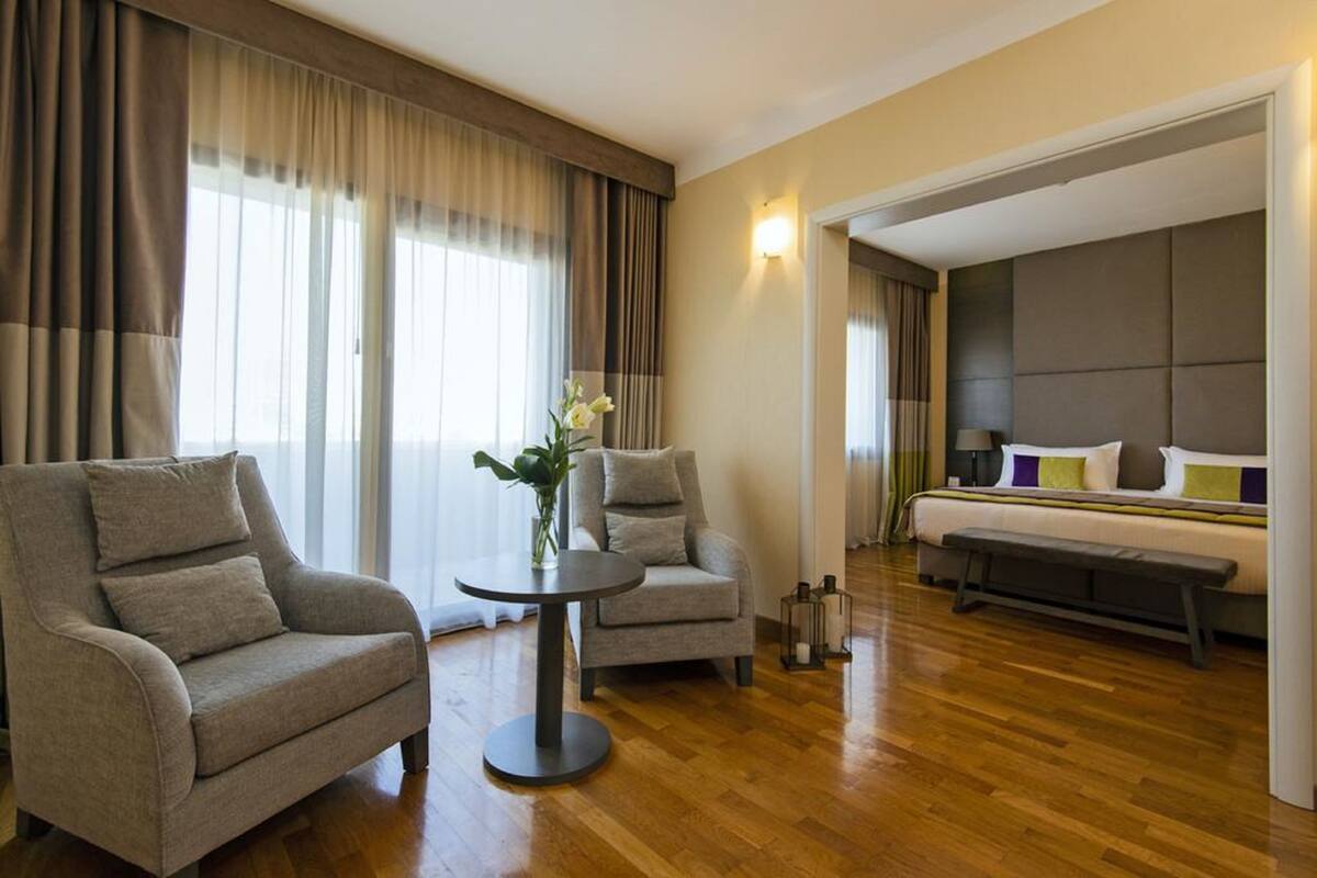 A hotel room with a bed, two armchairs, a small round table, and a vase with flowers.
