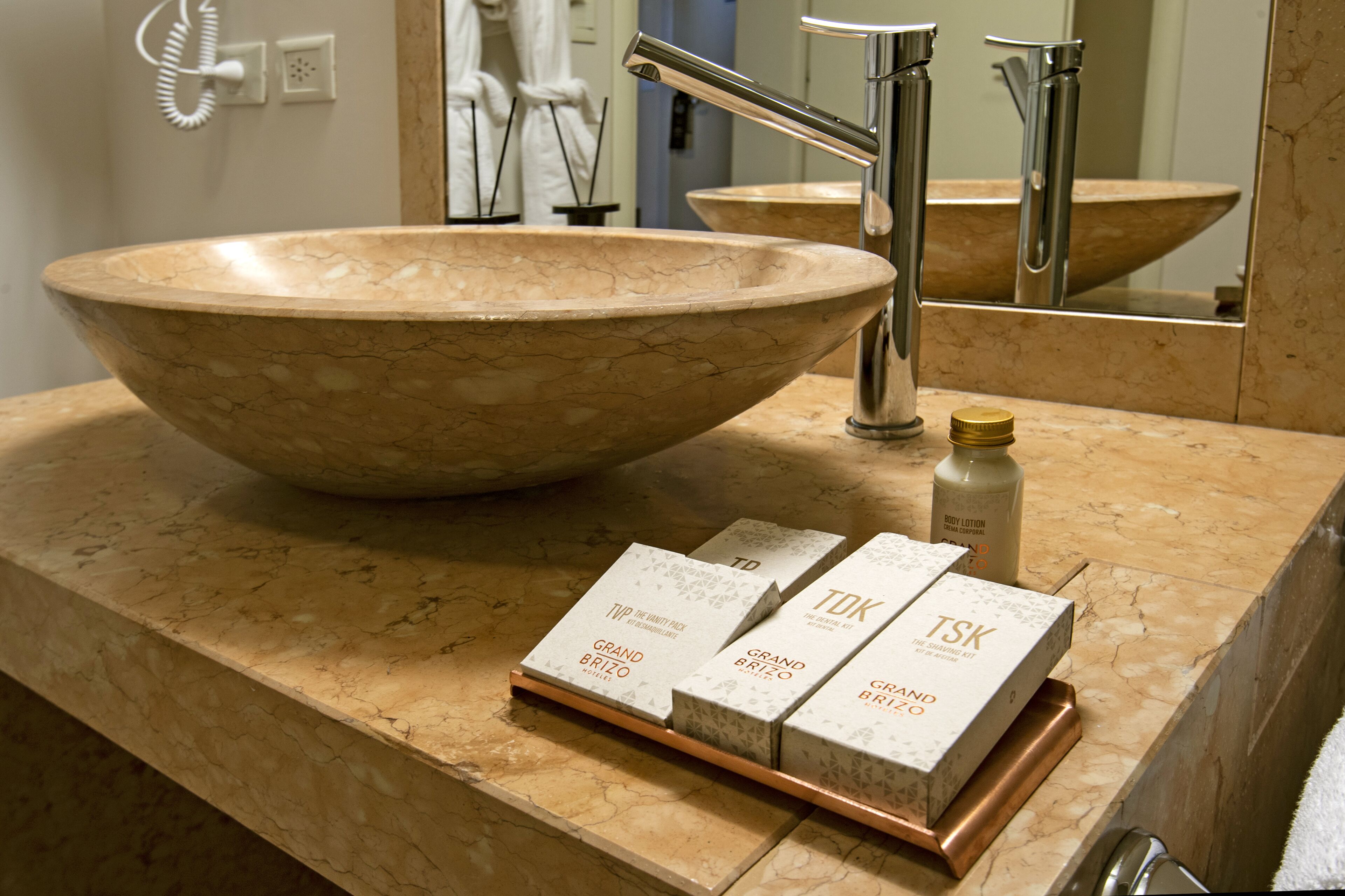 A bathroom with a large marble sink, a mirror, and three boxes of toiletries.