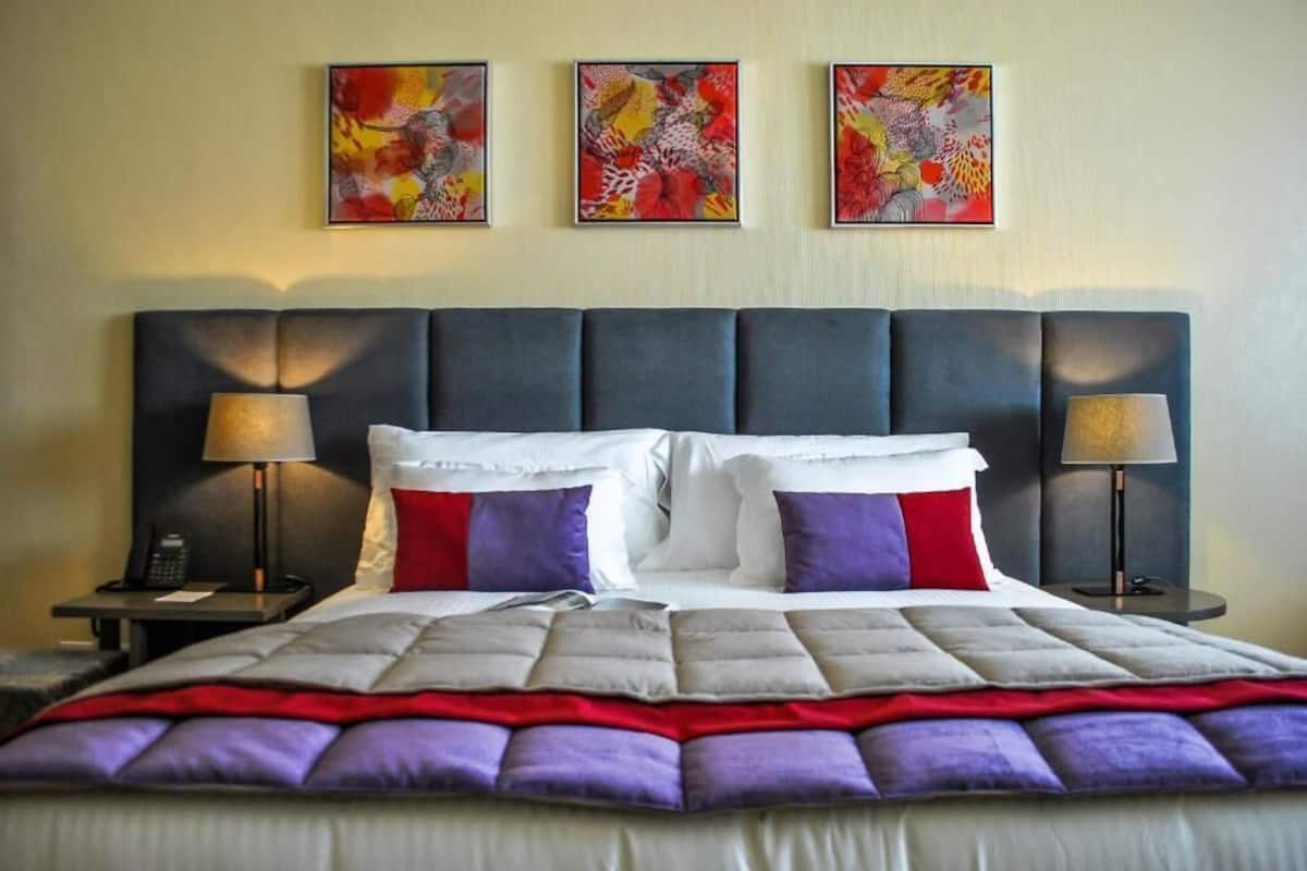 A hotel room with a large bed, two bedside tables, and three abstract paintings on the wall.