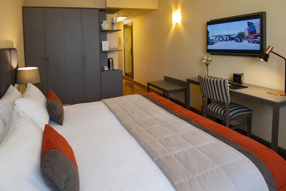 A hotel room with a large bed, a desk, a chair, and a television on the wall.