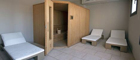 A compact room with a bed, two small seating areas, and a wooden wardrobe.