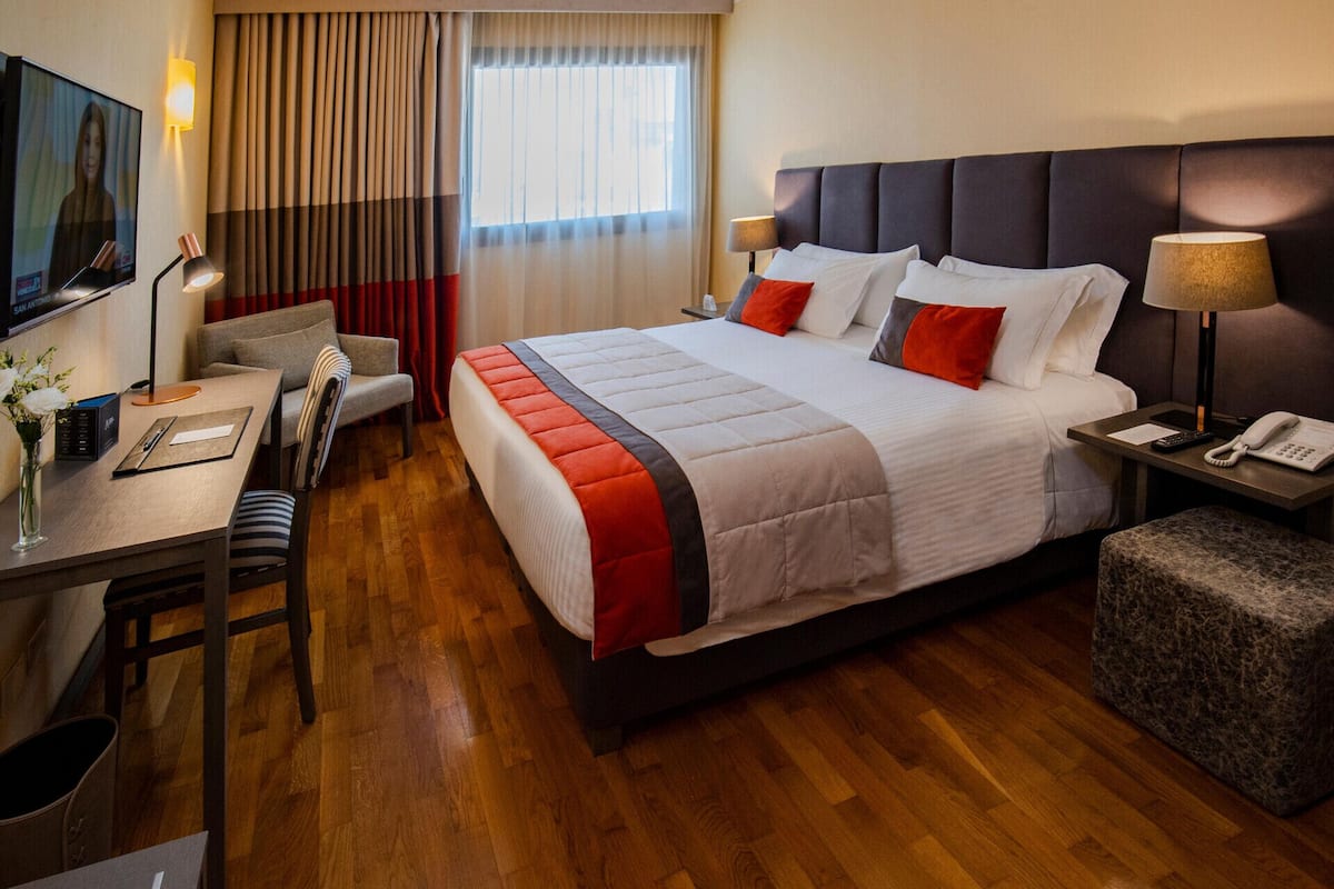 A hotel room with a bed, desk, chair, TV, and a window with curtains.