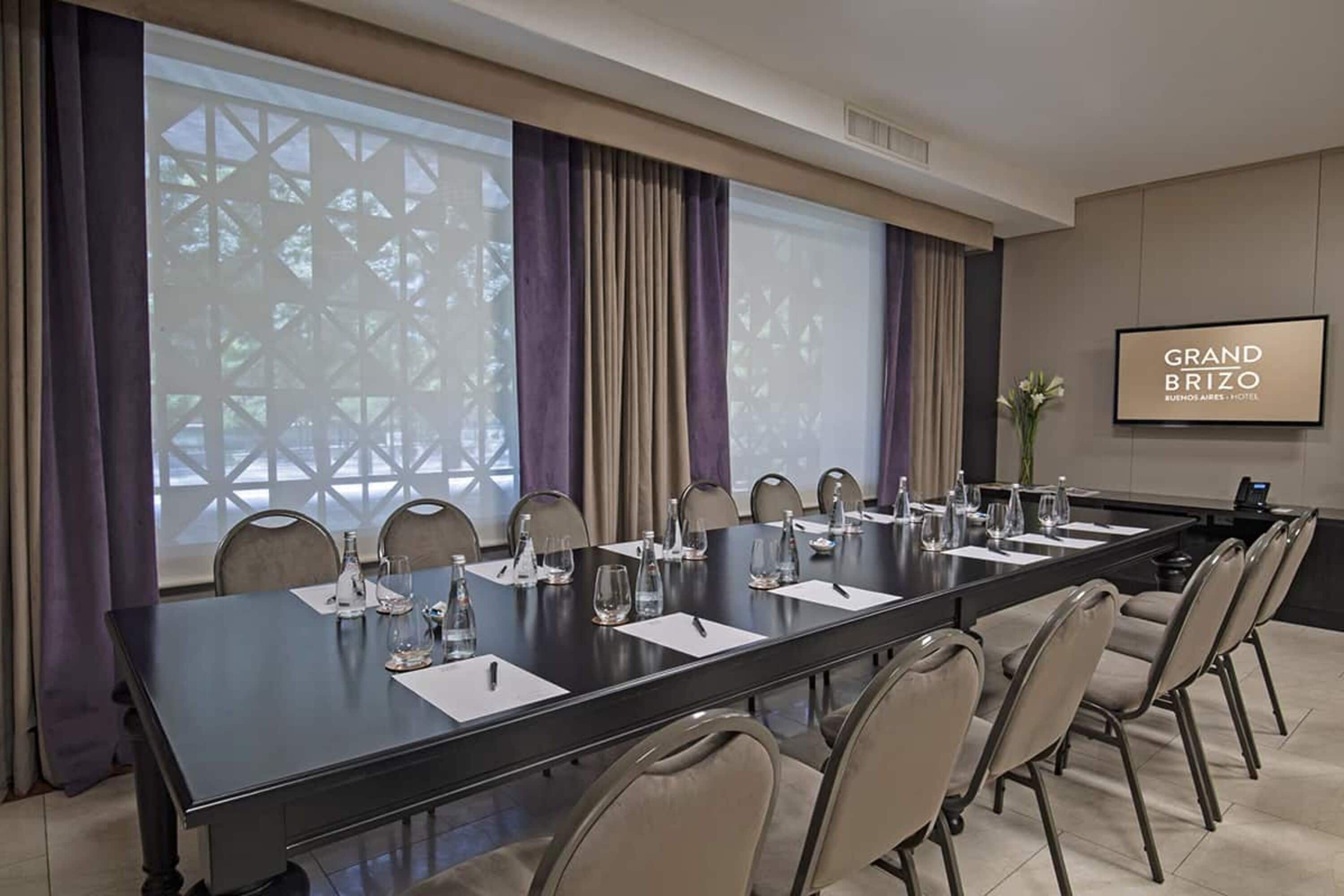 Une salle de conférence avec une longue table, des chaises et un écran de projection affichant le texte « GRAND BRIZO ».