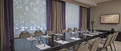 Un salón de conferencias con una larga mesa, sillas y una pantalla proyectora mostrando “GRAND BRIZO”.
