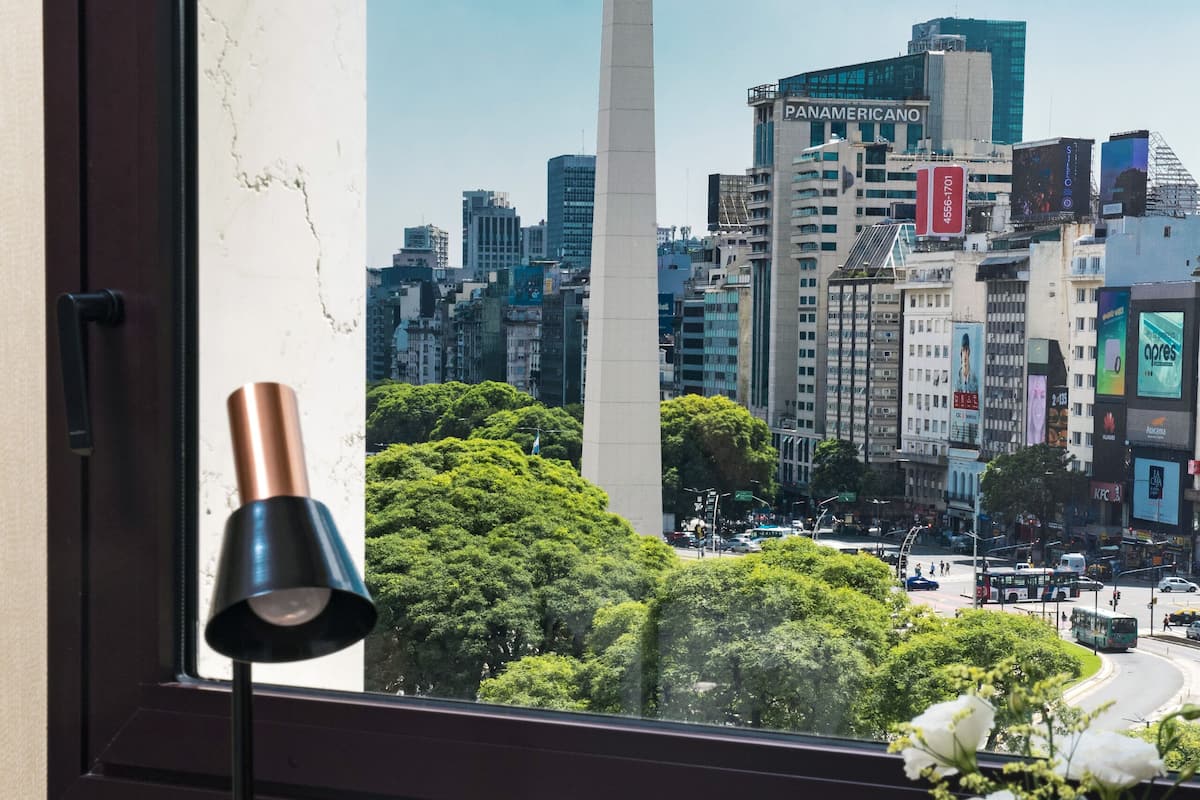 A desk with a lamp, a vase with flowers, and a view of a cityscape including a tall monument and modern buildings.