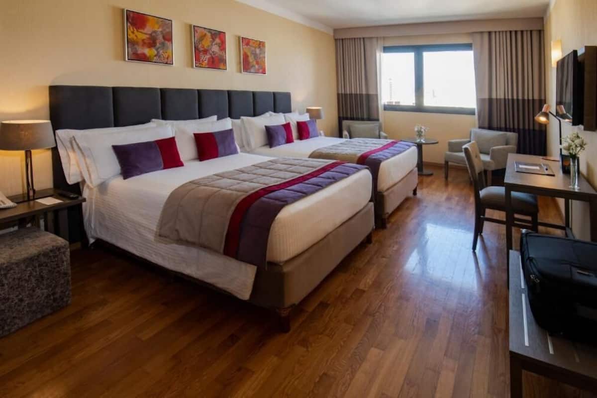 A hotel room with two beds, a desk, a chair, and a TV.